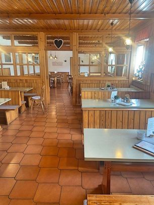 Ein leeres rustikales Restaurant mit Holzkabinen, gefliesten Böden und einer herzförmigen Dekoration. Tische und Stühle sind ordentlich angeordnet, und einige Topfpflanzen stehen auf den Tischen.