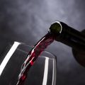 Eine Flasche Rotwein wird in ein Weinglas gegossen, der Moment wird mit einem dunklen Hintergrund eingefangen.