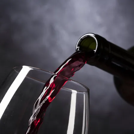 Eine Flasche Rotwein wird in ein Weinglas gegossen, der Moment wird mit einem dunklen Hintergrund eingefangen.