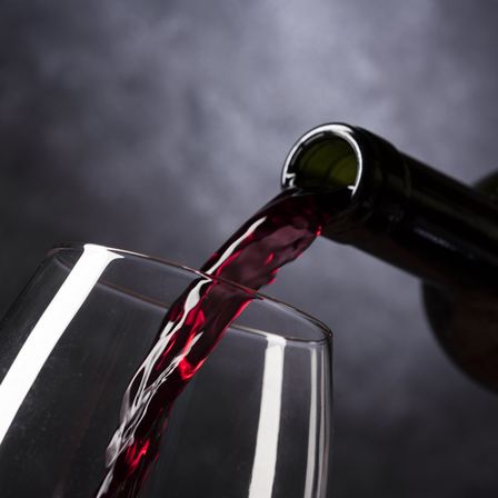 Eine Flasche Rotwein wird in ein Weinglas gegossen, der Moment wird mit einem dunklen Hintergrund eingefangen.