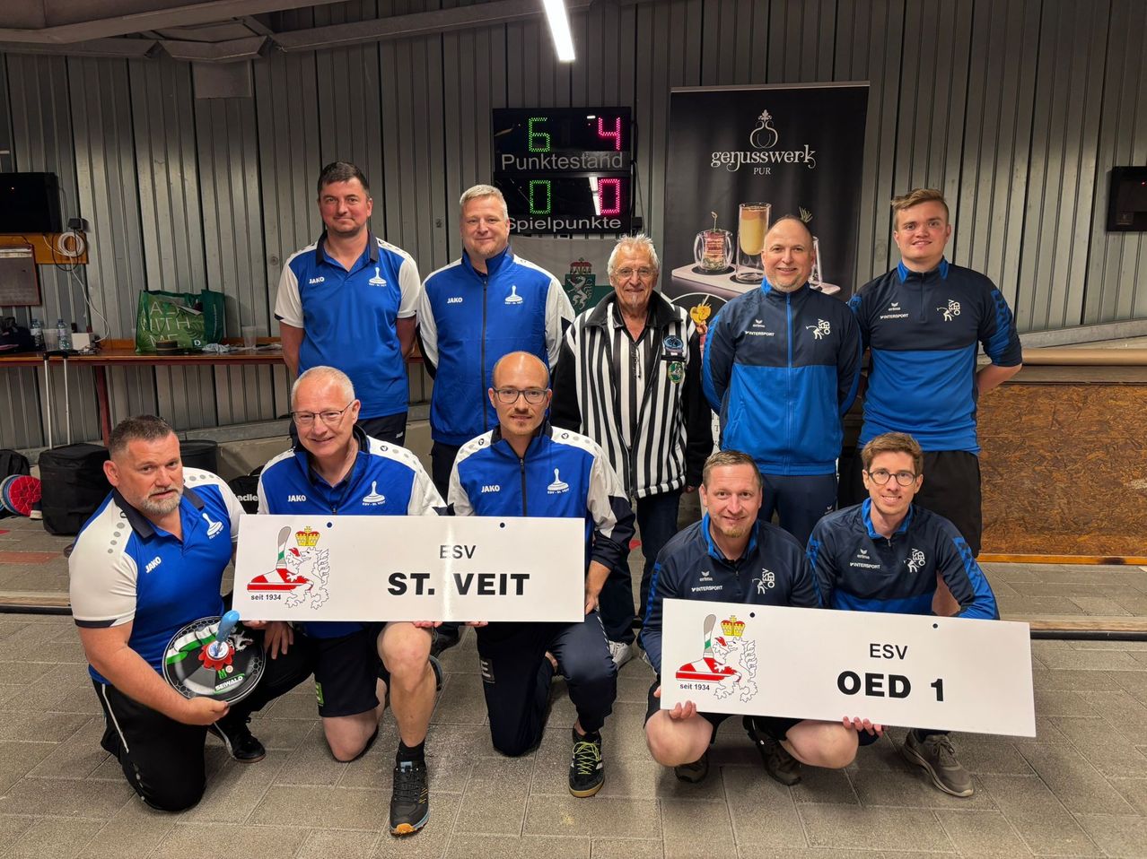 A group of men in blue and white uniforms pose for a photo. They hold signs with team names and a scoreboard in the background.