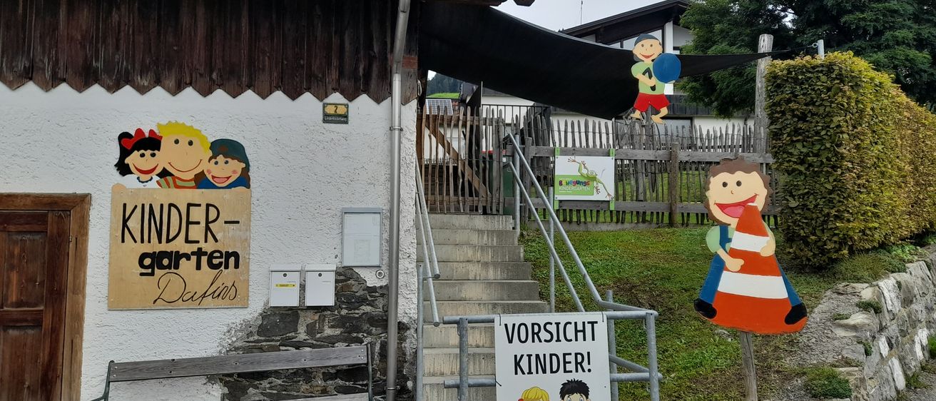 Der Eingang zu einem Kinderkindergarten mit Treppen, einem Handlauf und einem Schild, das 'Vorsicht Kinder!' und eine Zeichnung eines Mädchens und eines Jungen zeigt.