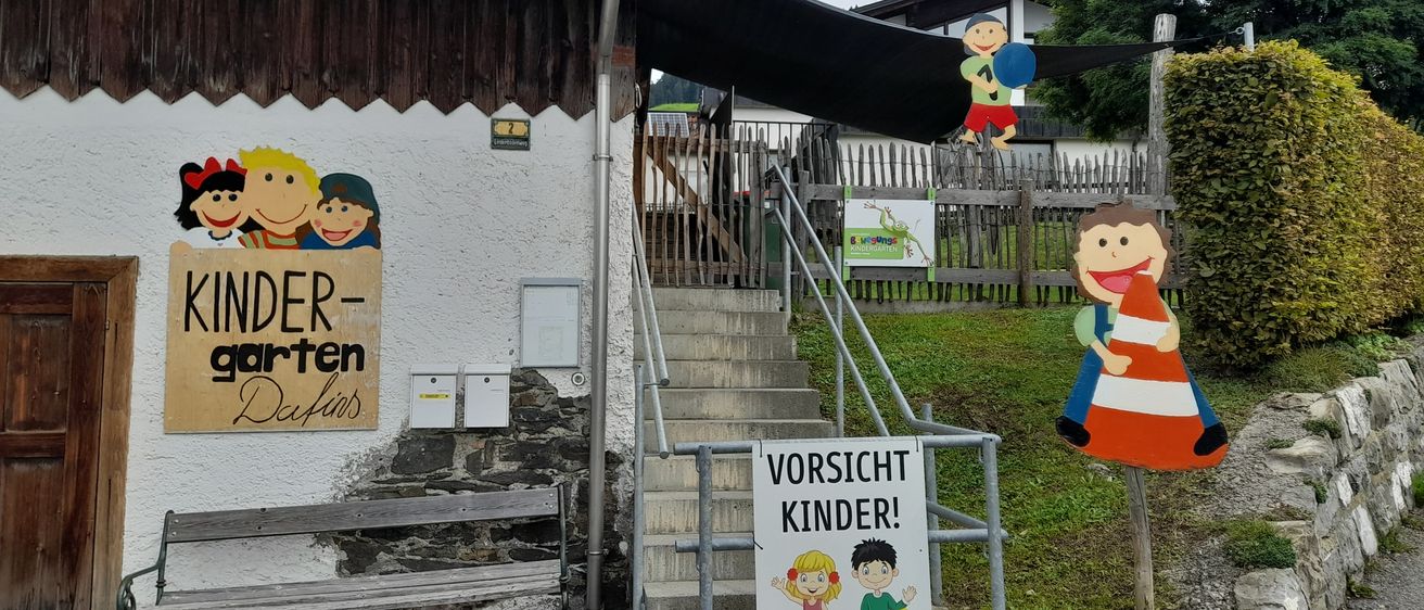 Der Eingang zu einem Kinderkindergarten mit Treppen, einem Handlauf und einem Schild, das 'Vorsicht Kinder!' und eine Zeichnung eines Mädchens und eines Jungen zeigt.