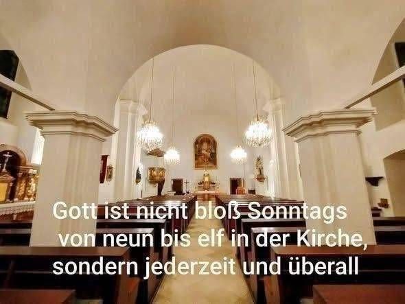 Ein Innenraum einer Kirche mit Reihen von Kirchenbänken, einem Mittelgang und dekorativen Kronleuchtern. Der Altar ist mit religiösen Symbolen und einem gerahmten Bild geschmückt. Der Text-Overlay lautet: 'Gott ist nicht nur sonntags von neun bis elf in der Kirche, sondern immer und überall.'