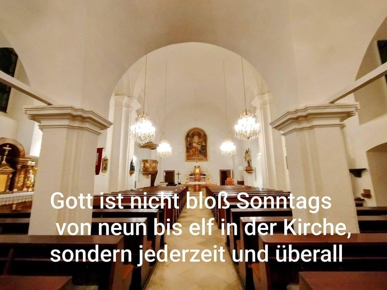 Ein Kircheninneres mit hölzernen Bänken, einem hohen Bogen und mehreren Kronleuchtern. Ein religiöses Gemälde hängt über dem Altar. Der Text lautet 'Gott ist nicht nur sonntags von neun bis elf in der Kirche, sondern jederzeit und überall.'