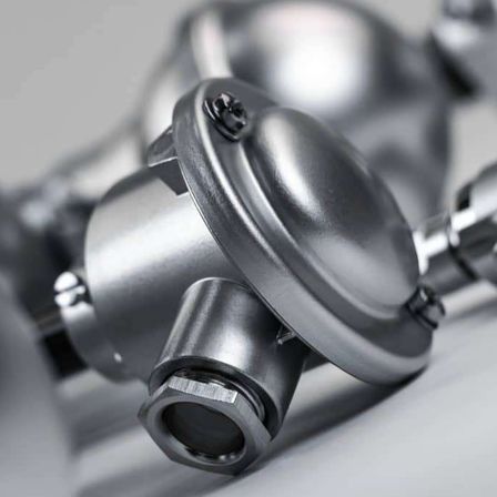 Nahaufnahme eines metallischen mechanischen Teils mit glänzender Oberfläche, mit einem sechseckigen Bolzen und runden Armaturen, auf einer grauen Oberfläche platziert.