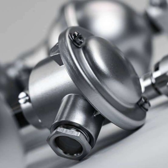 Nahaufnahme eines metallischen mechanischen Teils mit glänzender Oberfläche, mit einem sechseckigen Bolzen und runden Armaturen, auf einer grauen Oberfläche platziert.