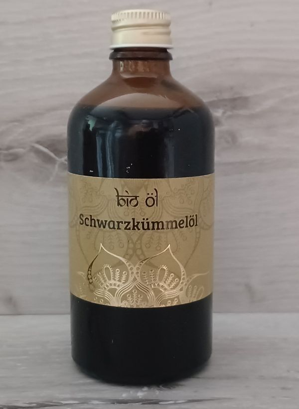 Eine Flasche Bio-Schwarzkümmelöl mit goldenem Etikett, auf einer weißen Marmoroberfläche platziert.