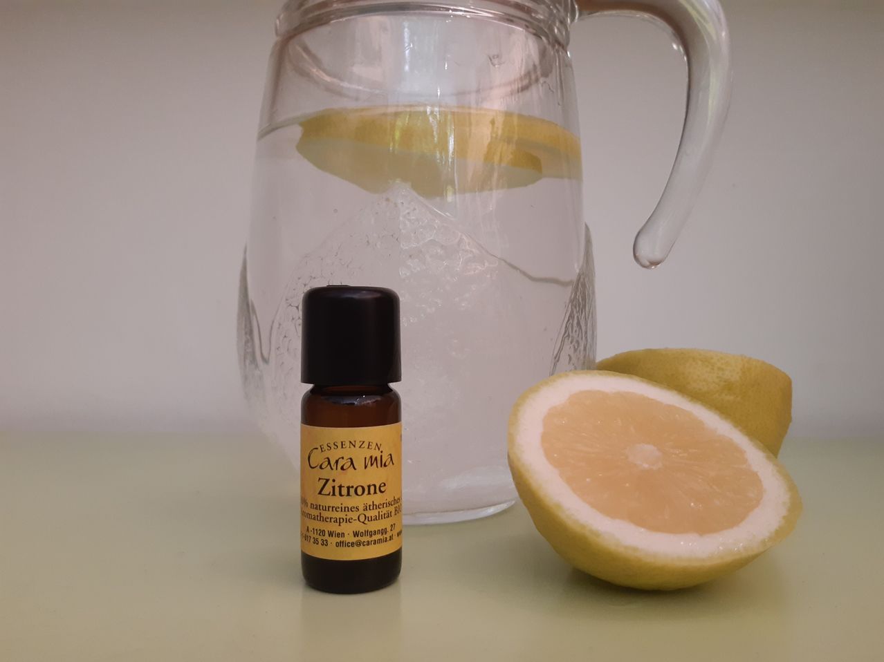 Eine Flasche Cara mia Zitrine ätherisches Öl steht neben einem Glaskrug mit Wasser und Zitronenscheiben. Eine geschnittene Zitrone ist rechts.