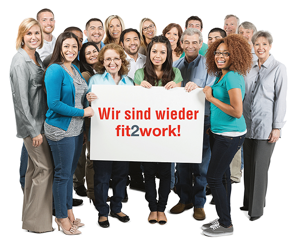 Eine Gruppe von verschiedenen Personen, die lächelnd zusammenstehen und ein weißes Schild mit dem Text 'Wir sind wieder fit2work!' in roten Buchstaben halten.