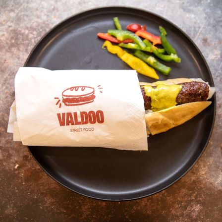 Ein schwarzer Teller hat einen Burger in einer Valdoo-Papierverpackung mit einigen farbigen Paprikaschoten an der Seite.