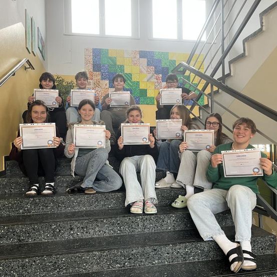 Eine Gruppe von Schülern posiert für ein Foto auf der Treppe, während sie Urkunden halten.