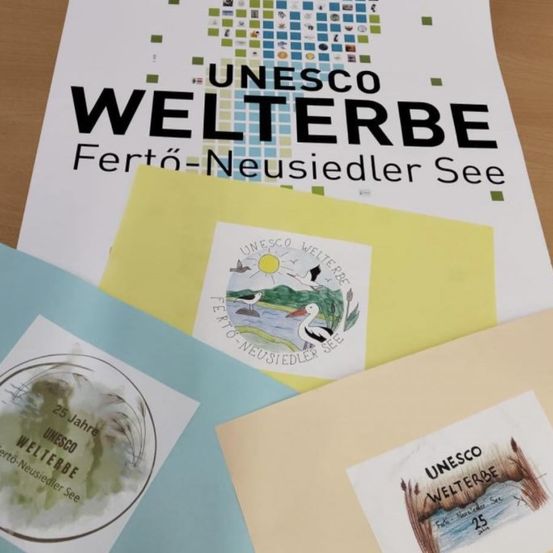 Ein Stapel von Dokumenten, darunter eines mit dem Titel 'UNESCO WELTERB' und andere mit verschiedenen Stempeln und Logos, liegt auf einer Holzoberfläche. Das oberste Dokument zeigt ein Design mit den Worten 'Ferto-Neusiedler See'.