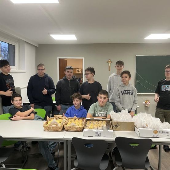 Eine Gruppe junger Männer steht hinter einem Tisch mit Körben und Kartons mit Essen. Sie scheinen für ein Foto in einem Klassenzimmer zu posieren.