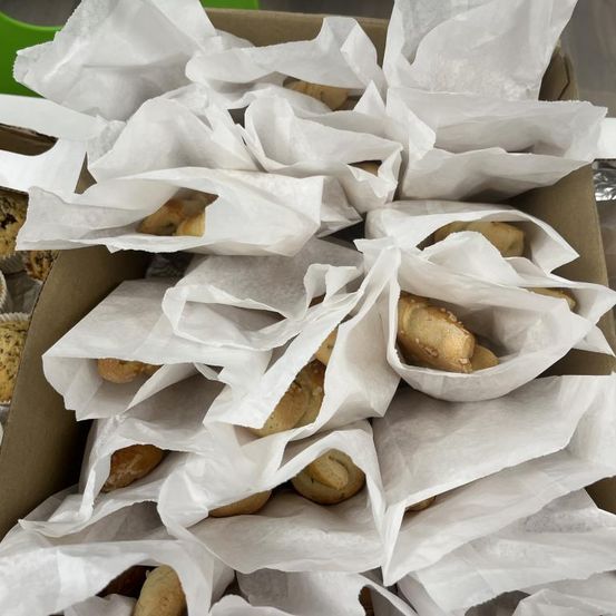 Eine Schachtel gefüllt mit mehreren weißen Papiertüten, jede mit einem goldbraunen Gebäck, möglicherweise Brezeln, auf einer grauen Oberfläche.
