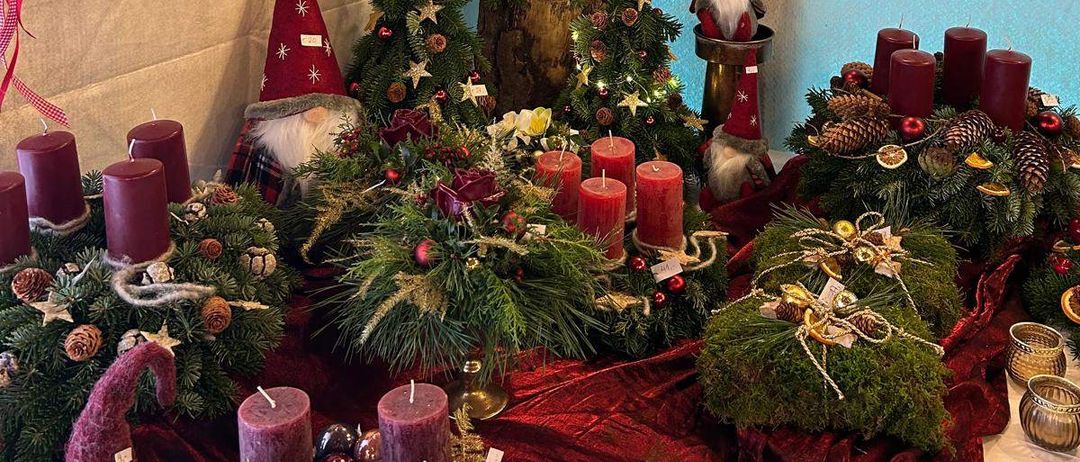 Eine Weihnachtsdekoration mit mehreren Kränzen und Ornamenten, die von der Decke hängen, einem kleinen Weihnachtsbaum und roten Kerzen, die auf dem Tisch angeordnet sind. Eine Weihnachtsmann-Figur steht in der Mitte.