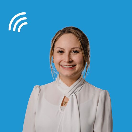 Eine lächelnde Frau in einem weißen Blusenhemd steht vor einem blauen Hintergrund mit einem Wi-Fi-Symbol in der oberen linken Ecke.