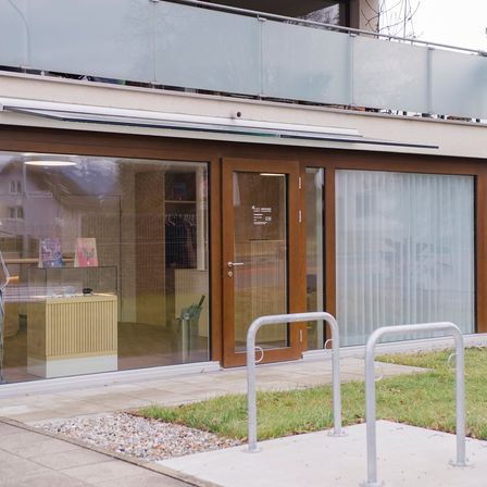 Das Äußere eines modernen Gebäudes mit Glastüren und -fenstern, einem kleinen Tisch und zwei Fahrradständern. Das Gebäude hat einen Balkon mit einer Metallbrüstung.