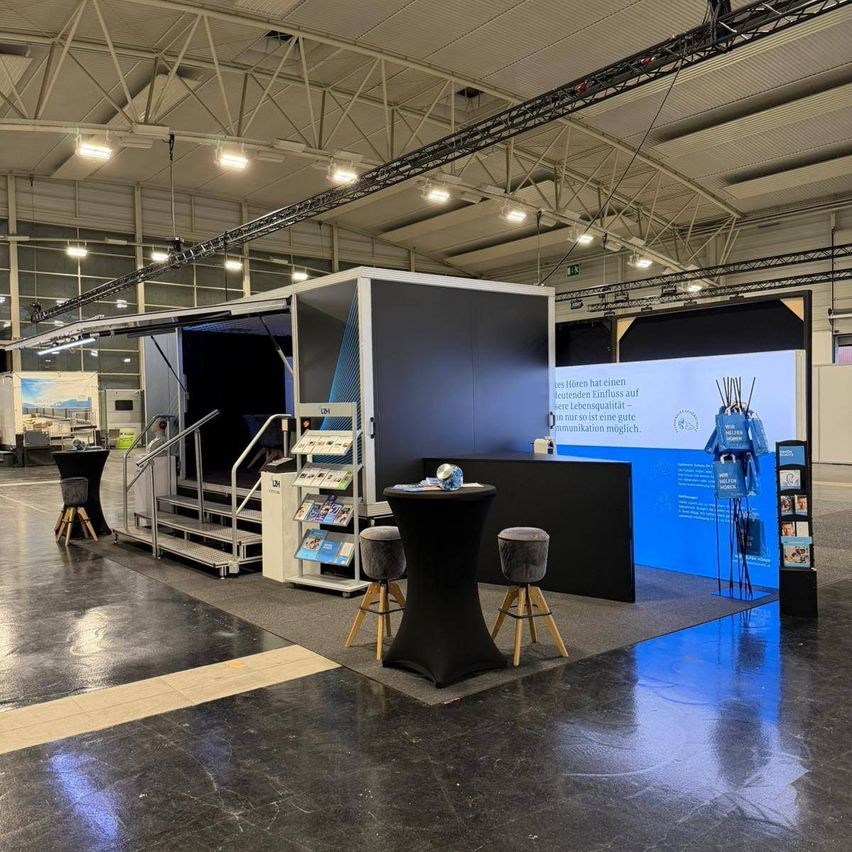 An indoor exhibit with a large blue wall and staircase. A large blue box with an open door and books on a stand. Two stools are in front of a desk with a globe. The floor is shiny and wet.
