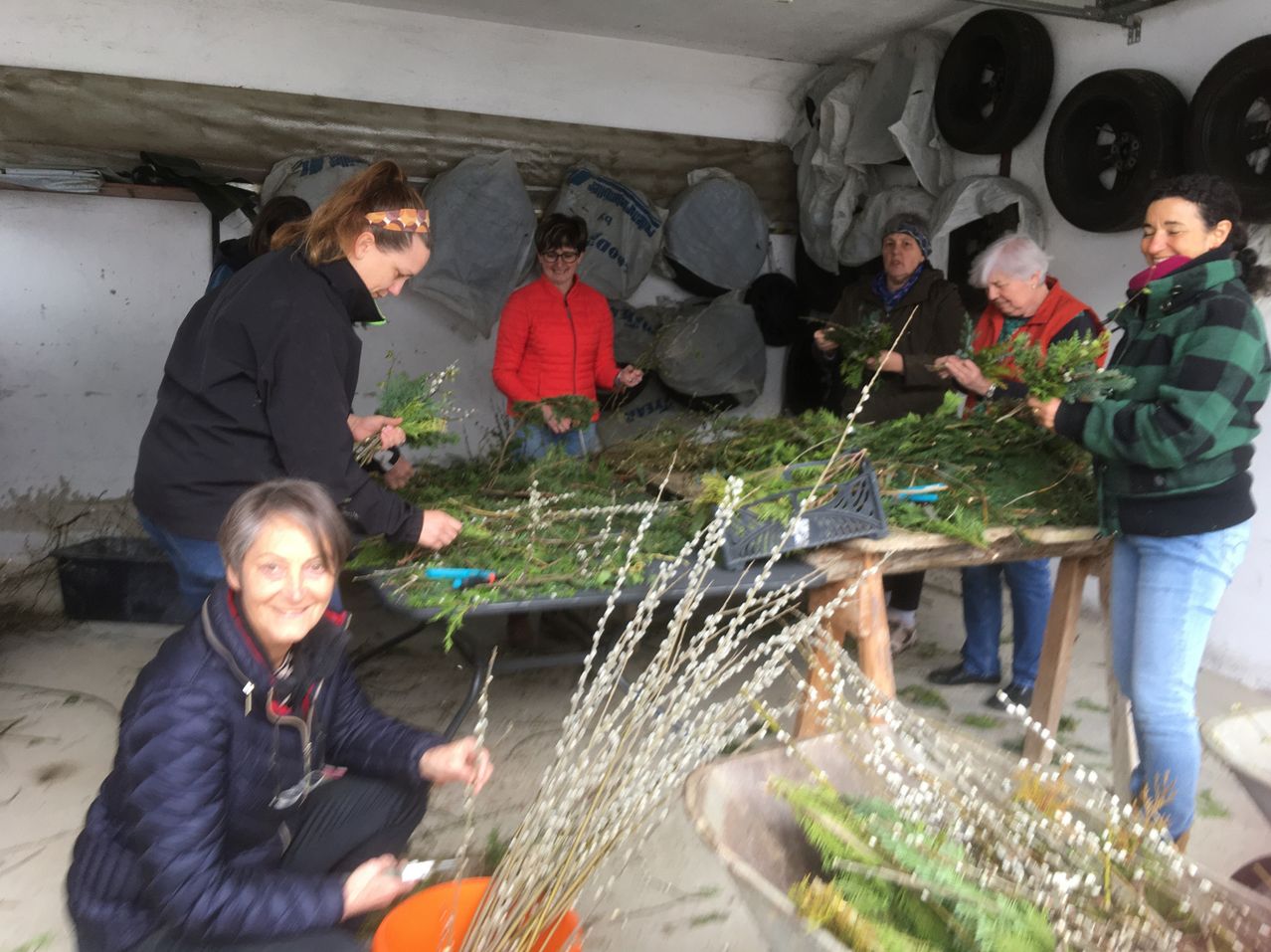 Eine Gruppe von Frauen arbeitet in einem Raum mit weißer Decke und weißen Wänden. Sie schneiden Äste von einer Pflanze. Die Äste liegen auf einem Tisch mit einem schwarzen Tablett. Die Frau vorne hält einen Ast.