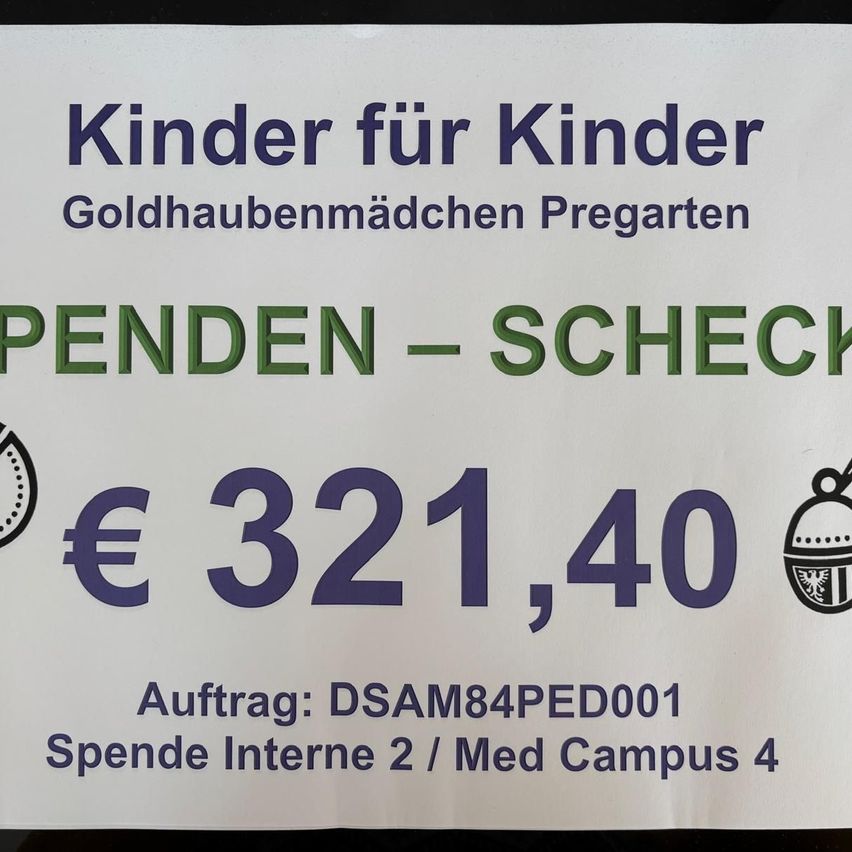 A white sign with blue and green text states 'Kinder für Kinder Goldhaubenmädchen Pregarten'. It includes a logo, a pending check symbol, an amount of 321.40 Euros, and a reference number DSAM84PED001. It mentions 'Spende Interne 2 / Med Campus 4'.
