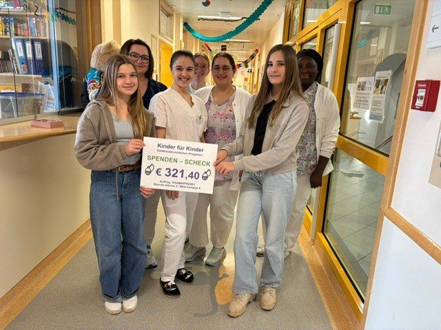 A group of young women holding a large check for 321.40 euros, standing in a hospital corridor with others, smiling.