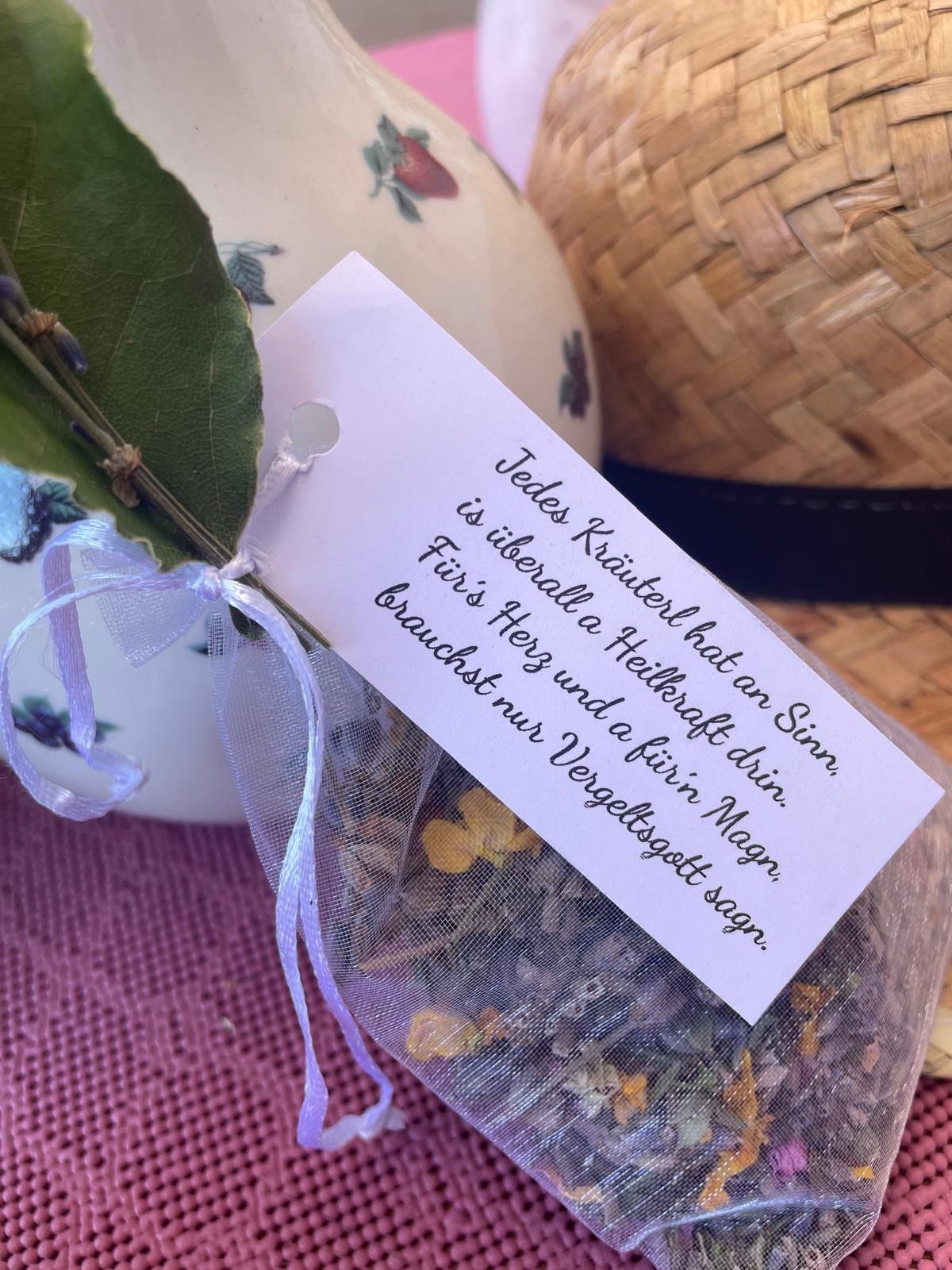 A small bag of dried herbs tied with a ribbon and a tag with German text is placed on a pink surface. The tag has a hole in the middle.