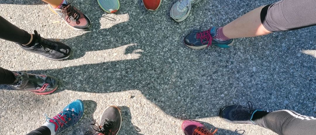 Eine Gruppe von Menschen in unterschiedlicher Laufbekleidung steht im Kreis. Sie tragen Turnschuhe in verschiedenen Farben, einige mit hellroten Akzenten.