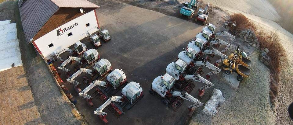 Eine Luftaufnahme einer Baustelle zeigt mehrere in einer Reihe geparkte Bagger, mit einem Gebäude namens E5 Rauch im Hintergrund.