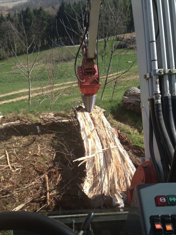 Ein Baumstamm wird von einer roten Maschine mit einer kreisförmigen Klinge auf einem Rasenfeld geschnitten.