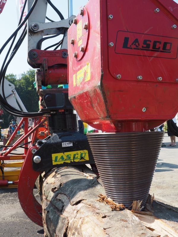 Eine rote Maschine mit dem Wort LASC darauf schneidet einen Baumstamm mit einer Kreissäge.