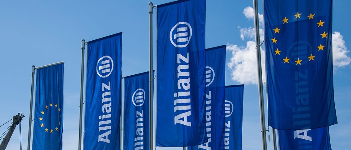 Mehrere blaue Banner mit weißem Text, der 'Allianz' liest und ein weißes Logo aufweist, sind an einem blauen Himmel mit Wolken auf Stangen aufgereiht.