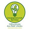 Ein grünes kreisförmiges Logo mit einer Glühbirne und Blättern darin, der Text lautet 'Energiegemeinschaft Bad Vöslau' und 'Naturstrom aus Bad Vöslau', mit einem Website-Link.