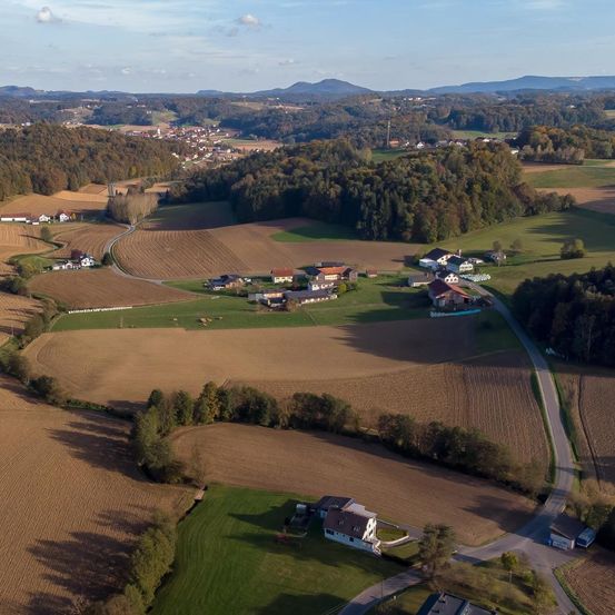 Luftaufnahme einer ländlichen Landschaft mit Feldern, Häusern und Bergen im Hintergrund.