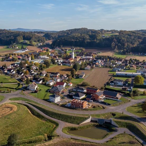 Luftaufnahme eines kleinen Dorfes mit vielen Häusern, einer Kirche und einem grünen Feld.