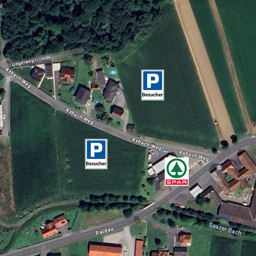 Eine Luftaufnahme eines ländlichen Gebiets mit Straßen und Häusern. Es gibt zwei Parkschilder, die auf Besucherparkplätze hinweisen. Eine Straße namens Axbach Weg kreuzt sich mit einer anderen Straße. Ein Gebäude mit einem grünen Logo ist sichtbar, und ein kleiner Bach ist im Hintergrund.