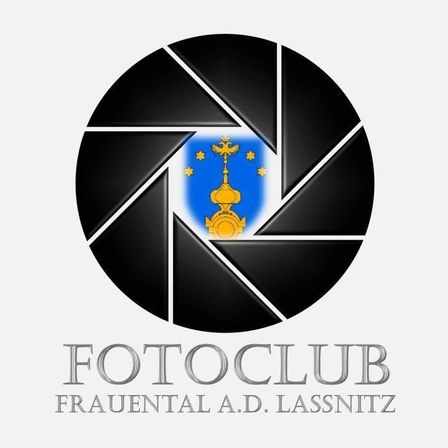 Das Logo des Fotoclub Frauental A.D. Lassnitz zeigt ein goldenes Kreuz und eine Kuppel in einem blauen Schild mit gelben Sternen, umgeben von einer schwarzen Kamerablende auf weißem Hintergrund.