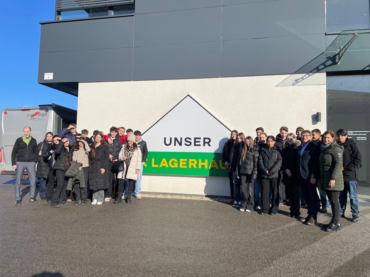 Eine Gruppe von Menschen posiert für ein Foto vor einem Gebäude mit einem Schild, das Unser Lagerhaus steht.