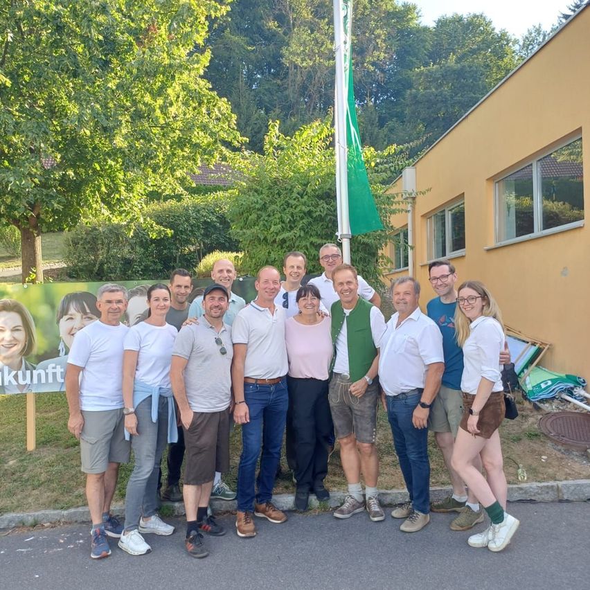 Eine Gruppe von Männern und Frauen steht vor einem Gebäude mit einem Banner und einer Fahne und posiert für ein Foto.