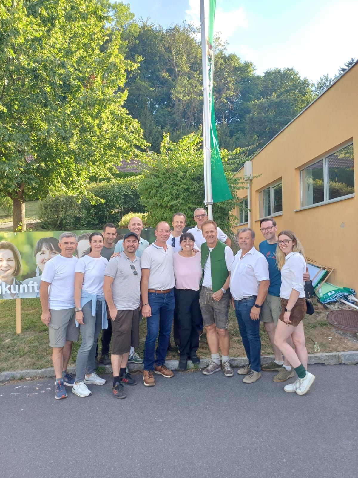 Wahlwerbung in Oberösterreich: Gruppe posiert vor Parteiplakat und gelbem Gebäude