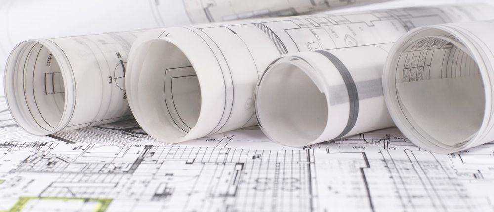 Architektonische Baupläne auf einem Schreibtisch aufgerollt, mit Grundrissen und Schnitten, Linien und Markierungen.