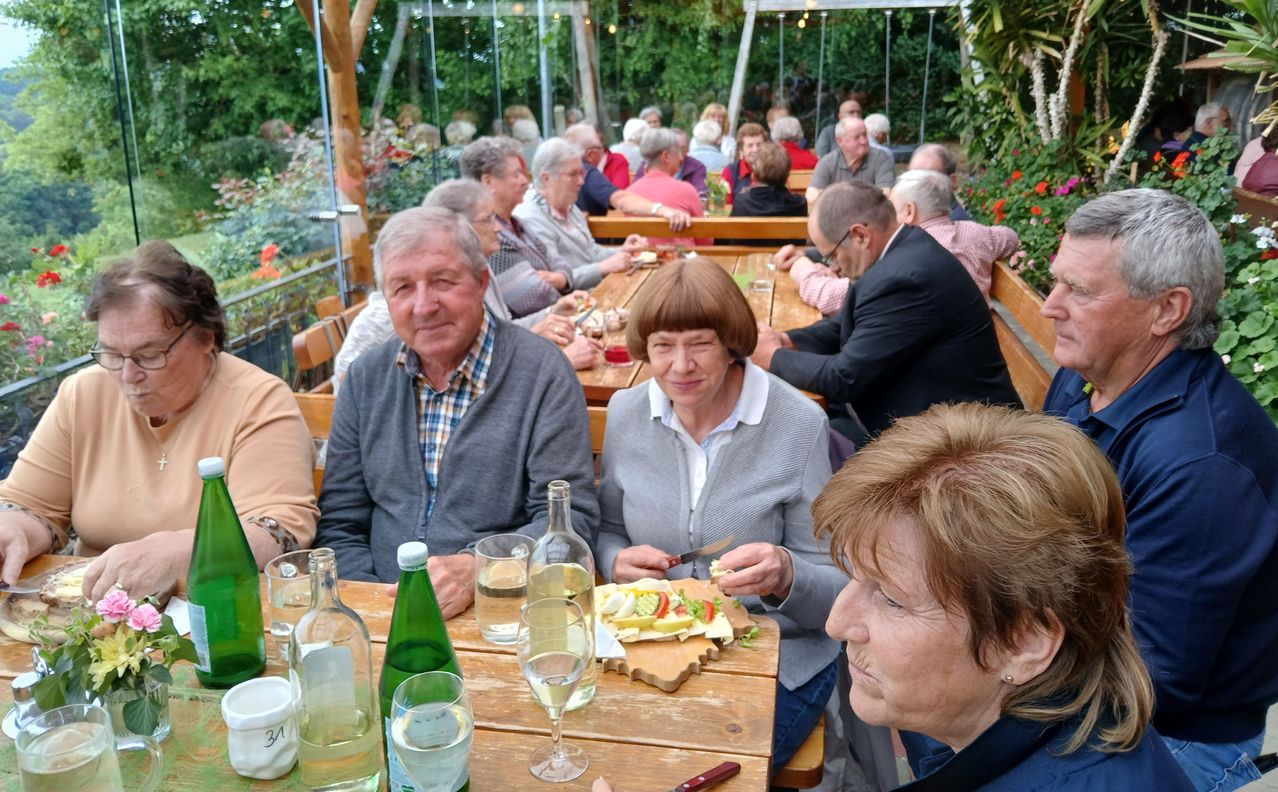 Eine Gruppe älterer Menschen sitzt an einem Tisch in einem Außenrestaurant und genießt Essen und Getränke.