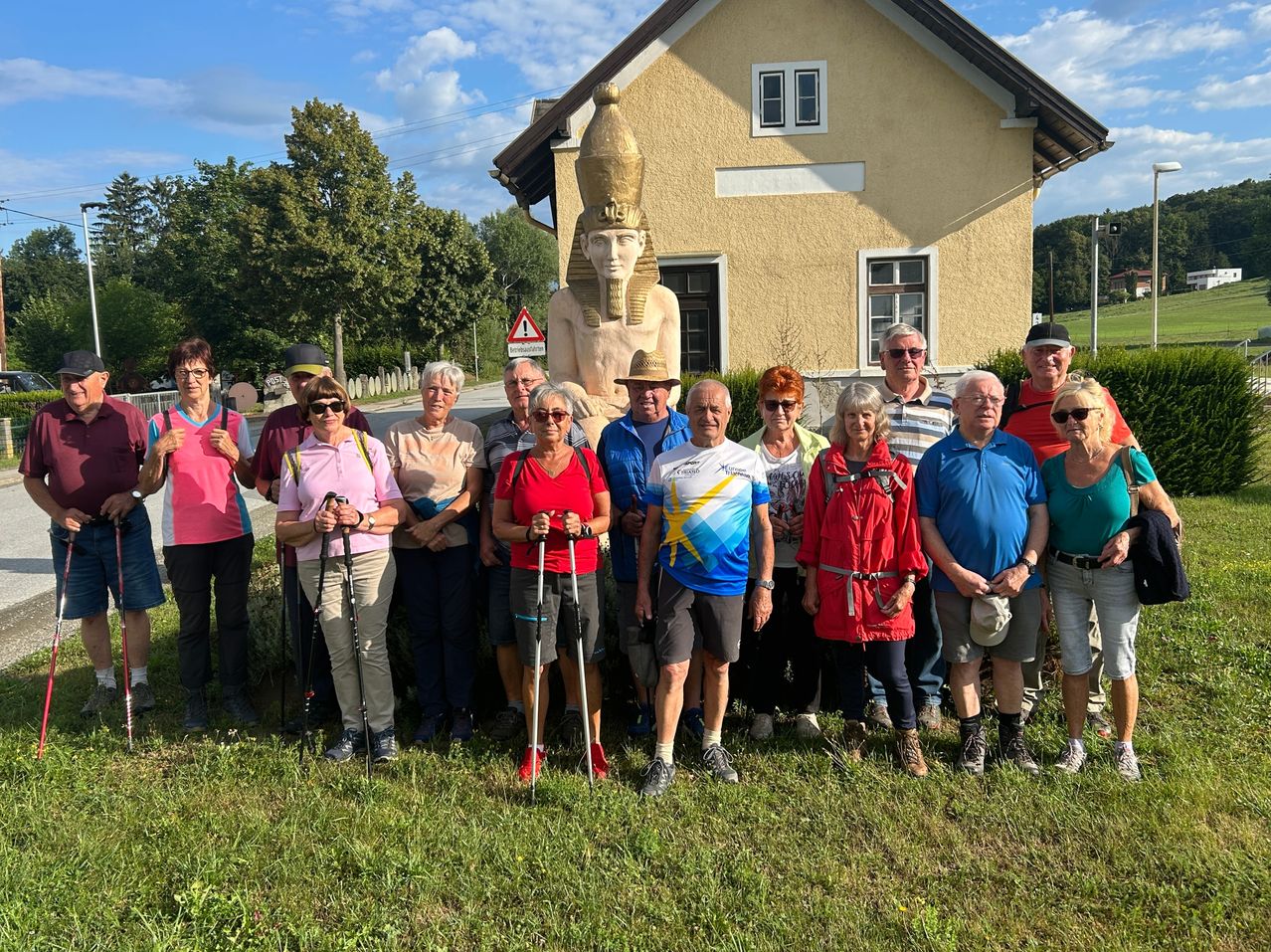 Eine Gruppe von Wanderern steht vor einem Haus mit einer großen Statue eines ägyptischen Pharaos im Hintergrund.