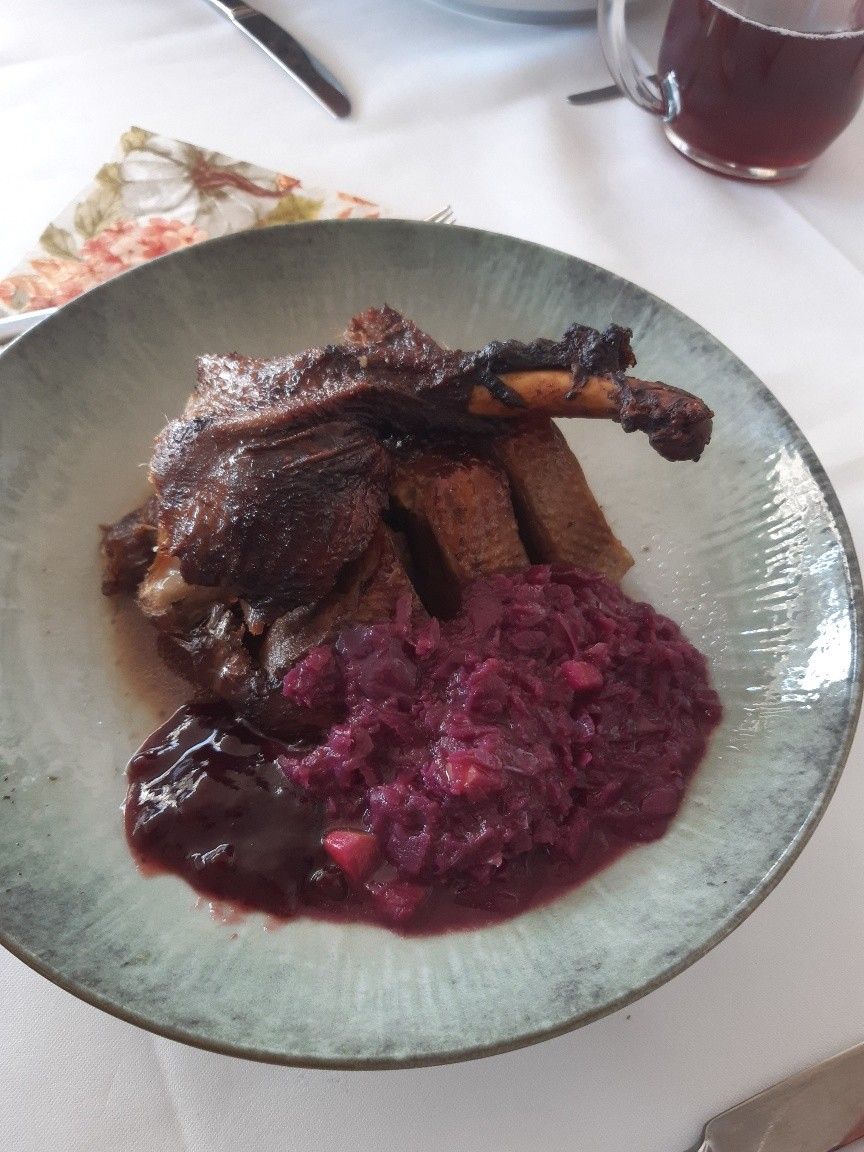 Ein Teller mit einem gebratenen Lammkeule, Rotkohl und einer sauceartigen Soße. Das Lamm ist dunkelbraun und sieht saftig aus. Der Rotkohl ist fein gehackt.
