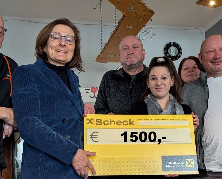Eine Gruppe von Menschen steht in einem Raum, hält einen großen Scheck über 1500 Euro und posiert für ein Foto.
