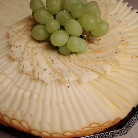 Eine Platte mit fächerförmig geschnittenem Käse, gekrönt von grünen Trauben und Kräutern.