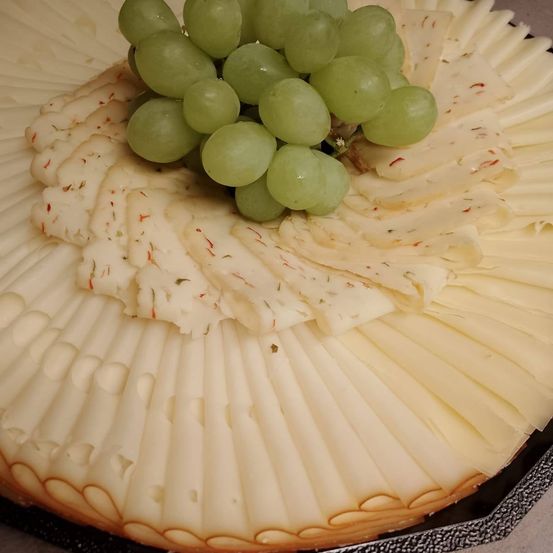 Eine Platte mit fächerförmig geschnittenem Käse, gekrönt von grünen Trauben und Kräutern.