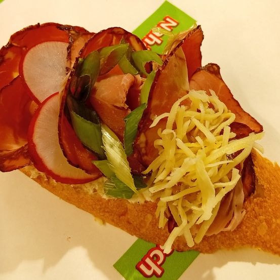 Ein Sandwich mit geschnittenem Schinken, Käse und Radieschen auf einem weißen Hintergrund mit einem grünen und roten Design.