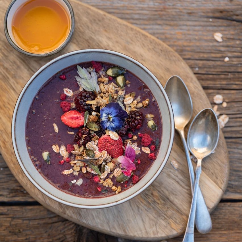 Eine Schüssel mit Smoothie mit Beeren und Granola auf einer Holzoberfläche mit einer Tasse Honig.