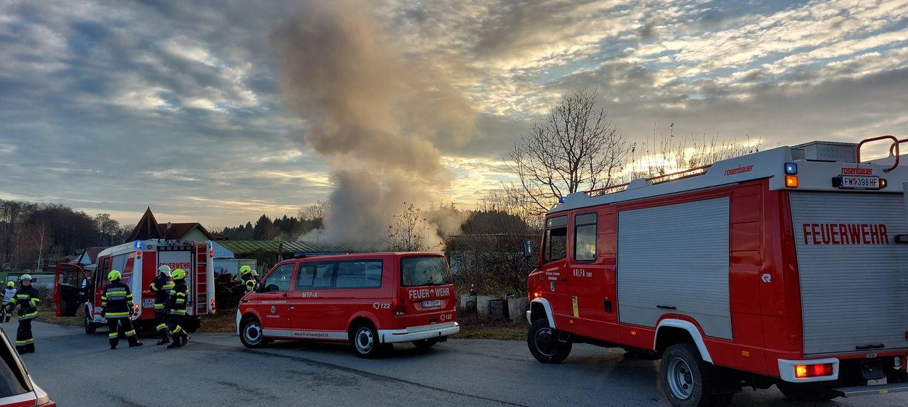 Ein roter Feuerwehrwagen mit der Aufschrift 'Feuerwehr' steht auf der Straße, mit einem rauchigen Himmel im Hintergrund.